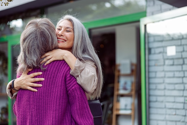 Mulher asiática sênior abraçando um amigo em uma rua da cidade moderna