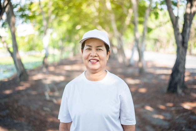 Mulher asiática sênior em pé e sorrindo após o treino de pausa em um parque público. Conceito de mulher idosa saudável