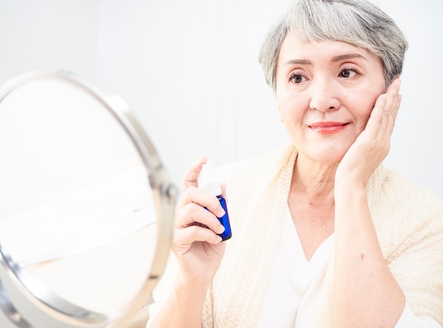 Mulher asiática sênior feliz aplicando loção no rosto.