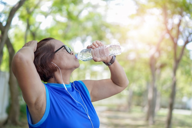 Mulher asiática sênior, garrafa de água potável após o exercício de treino