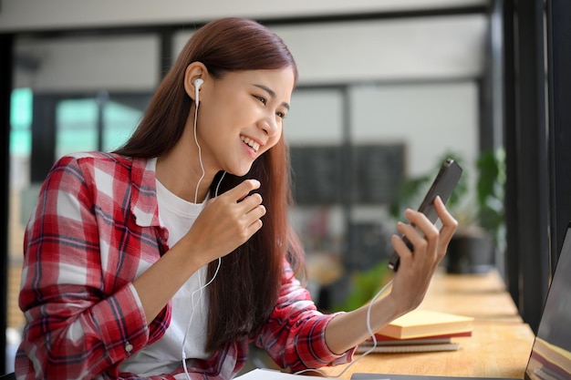 Mulher asiática senta-se na cafeteria usando fones de ouvido e videochamadas com seus amigos