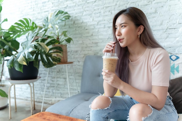 Mulher asiática sentada e bebendo café gelado e sorrindo alegremente