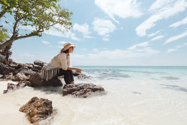Mulher asiática sentada na praia, olhando o mar incrível e curtindo com a beleza natural em suas férias. Conceito de férias de verão.