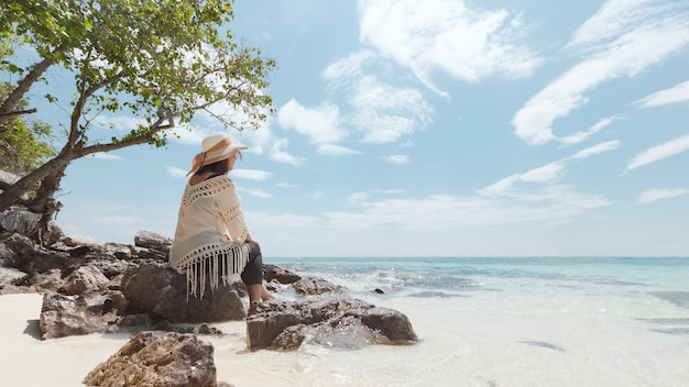 Mulher asiática sentada na praia, olhando o mar incrível e curtindo com a beleza natural em suas férias. Conceito de férias de verão.
