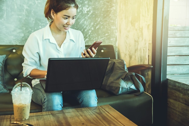 Mulher asiática sentada no sofá com o laptop