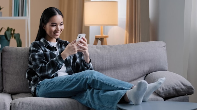Mulher asiática sentada no sofá em casa relaxando assistindo feed de notícias nas mídias sociais escolhendo