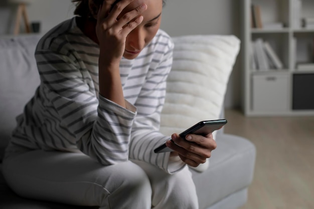 Foto mulher asiática sentada no sofá olhando para o telefone sentindo-se desapontada, triste, chateada mulher sofre de problemas de saúde mental