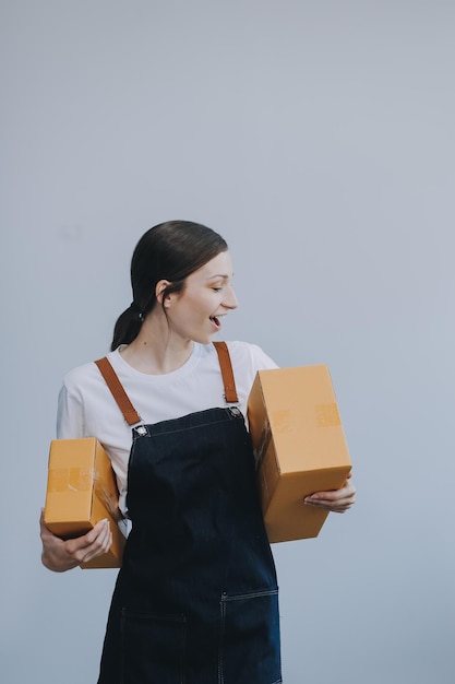 Mulher asiática sorridente em roupas casuais segurando um modelo de caixa de papelão enquanto está de pé contra um conceito de negócio de transporte de fundo branco isolado