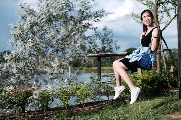 Mulher asiática sorridente relaxando em um balanço no parque