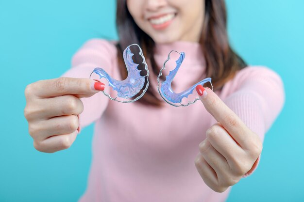 Mulher asiática sorridente segurando retentor ortodôntico em fundo de tela azul. Cuidados dentários e dentes saudáveis.