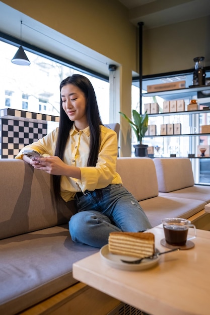 Foto mulher asiática sorridente sentada no banco na mesa do café lendo algo em seu smartphone