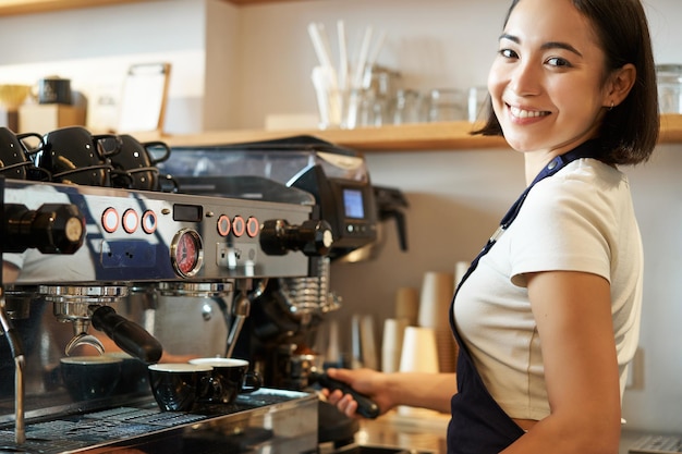 Mulher asiática sorridente trabalhando em café usando máquina de café para pedidos de cappuccino expresso em pé