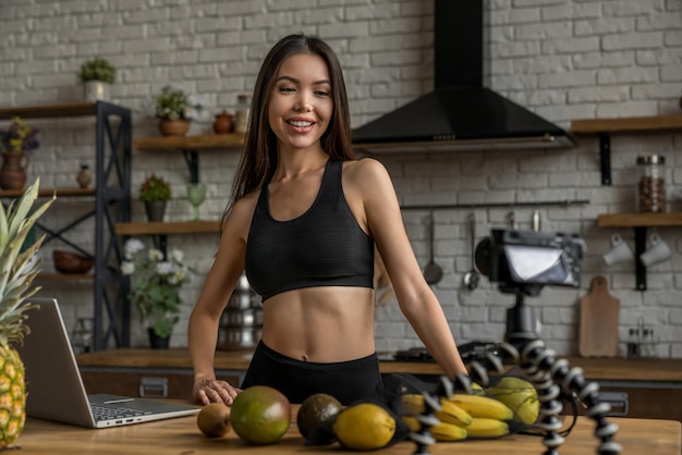 Mulher asiática sorridente trabalhando no conceito de blogueiro de comida com frutas e legumes na cozinha