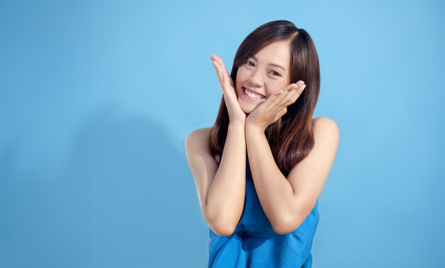 Foto mulher asiática sorridente usando as mãos para tocar seu rosto usando uma toalha em um fundo azul imagem de um modelo feminino com o conceito de saúde e limpeza do corpo