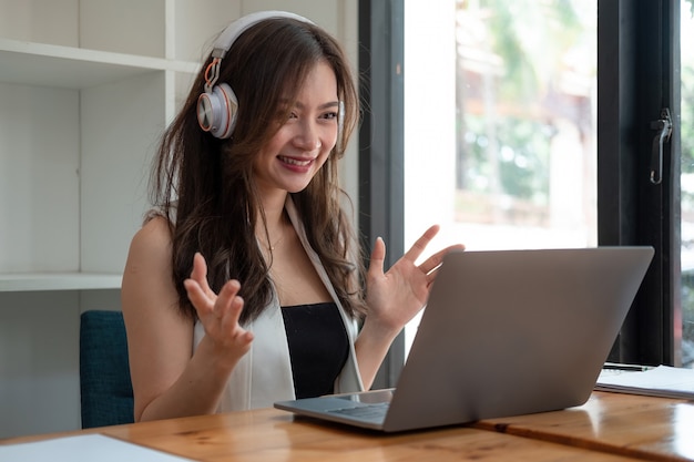 Foto mulher asiática sorridente usando fone de ouvido se comunicando com o cliente por vídeo