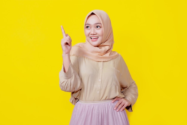Foto mulher asiática sorridente usando hijab com o dedo apontando isolado no fundo do banner amarelo claro