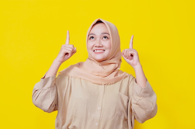 Foto mulher asiática sorridente usando hijab com o dedo apontando isolado no fundo do banner amarelo claro