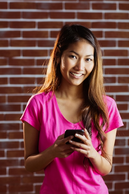 Mulher asiática sorridente usando smartphone na parede de tijolo