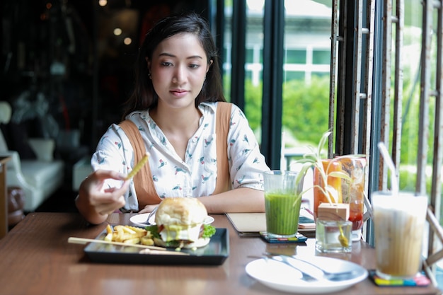 Mulher asiática sorrindo comendo hambúrguer em um café