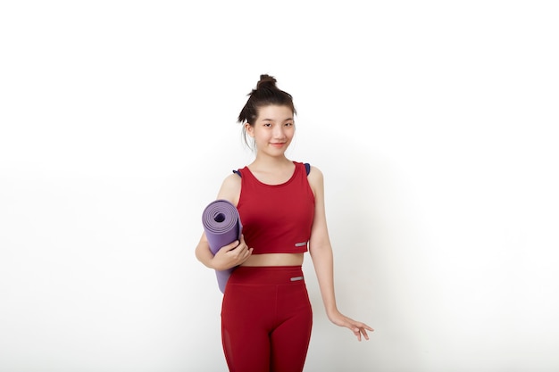 Mulher asiática tailandesa de exercícios físicos pronta para o treino em pé segurando um tapete de ioga