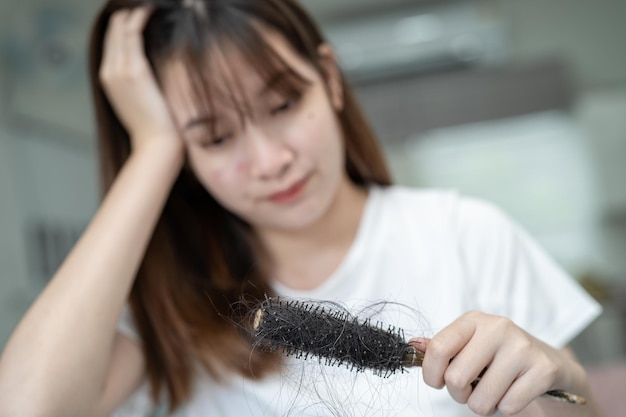 Mulher asiática tem problema com queda de cabelo longa anexada à escova de pente
