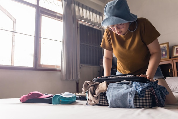 Mulher asiática tenta encaixar tudo na bagagem com pertences difíceis, como óculos de sol, bolsa de cosméticos de câmera polaroid e bolsa pequena Embalagem para sair de férias