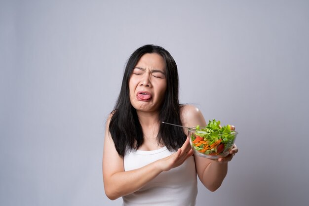 Mulher asiática tentando comer salada para dieta isolada sobre uma parede branca. estilo de vida saudável com conceito de comida limpa.