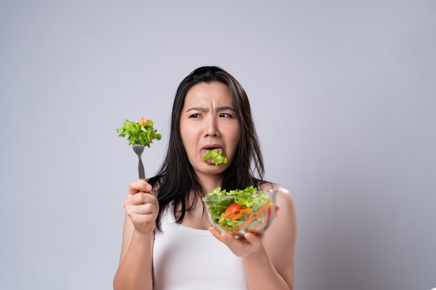 Mulher asiática tentando comer salada para dieta isolada sobre uma parede branca. estilo de vida saudável com conceito de comida limpa.