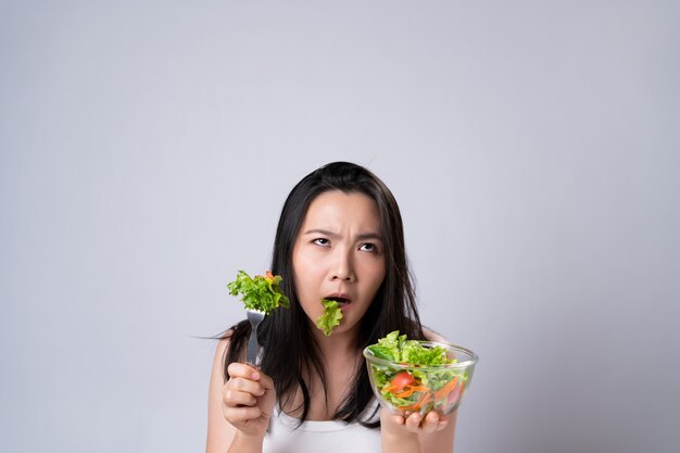 Mulher asiática tentando comer salada para dieta isolada sobre uma parede branca. estilo de vida saudável com conceito de comida limpa.