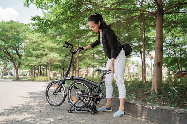 Mulher asiática, tentando dobrar sua bicicleta dobrável