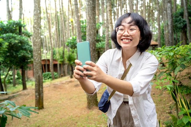 Mulher asiática tirando um autorretrato usando um telefone celular na floresta