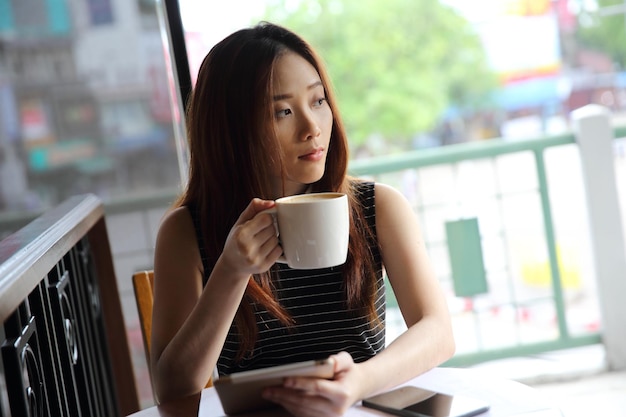 Mulher asiática tomando café com tablet