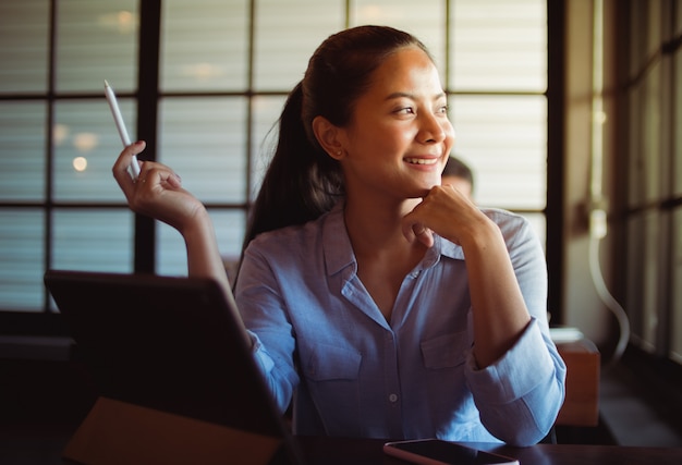 Mulher asiática tomando café e trabalhando com o computador portátil no café