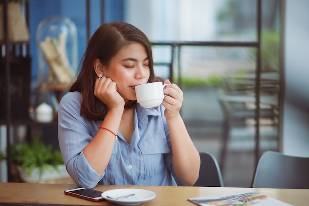 Foto mulher asiática tomando café na cafeteria café e usando telefone celular