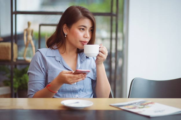 Mulher asiática tomando café na cafeteria café e usando telefone celular