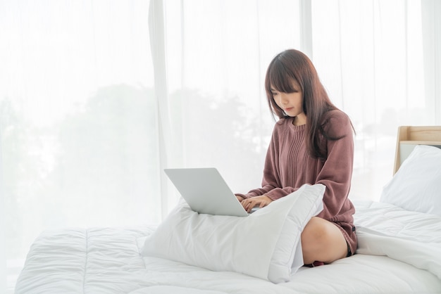 Mulher asiática trabalhando com laptop na cama em casa