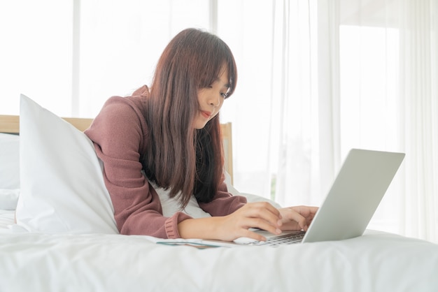 Mulher asiática trabalhando com laptop na cama