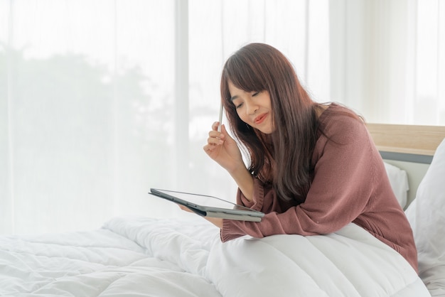 Mulher asiática, trabalhando com tablet na cama