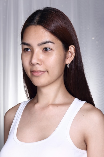 Mulher asiática transgênero antes de maquiagem estilo de cabelo morena. sem retoque, rosto fresco com pele bonita e macia. Fundo cinza com iluminação de estúdio, retrato
