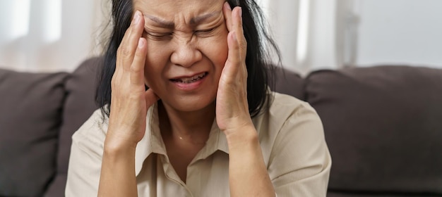 Mulher asiática triste de meia-idade tocando testa com dor de cabeça sofrendo de enxaqueca mulher asiática madura se sentindo doente ou depressão