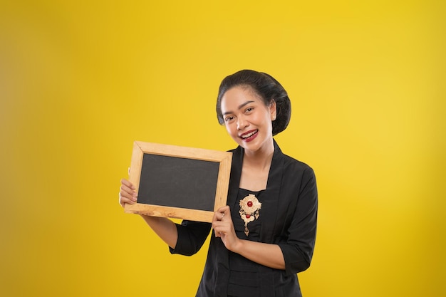 Mulher asiática usando kebaya sorrindo enquanto segura um pequeno quadro negro