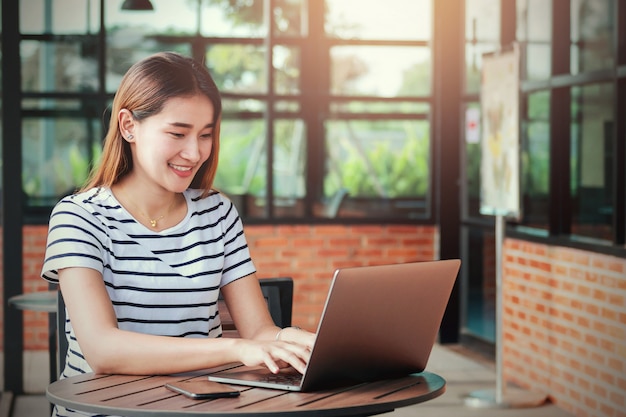 Mulher asiática usando laptop com feliz e sorrir no café café para trabalhar on-line