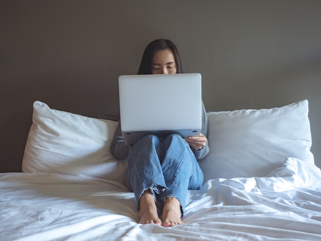 Mulher asiática usando laptop na cama