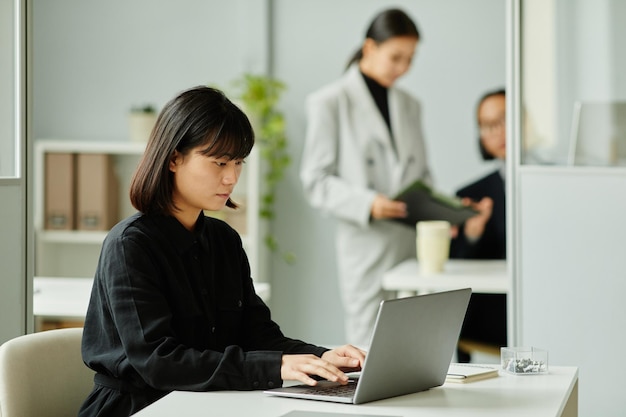 Mulher asiática usando laptop na vista lateral do escritório