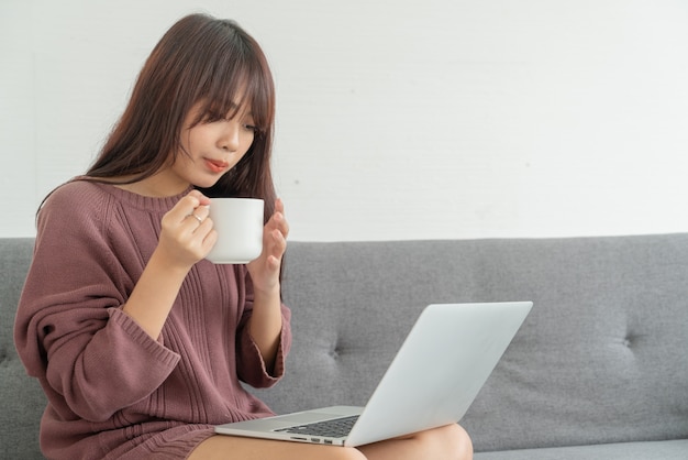 Mulher asiática usando laptop no sofá na sala de estar