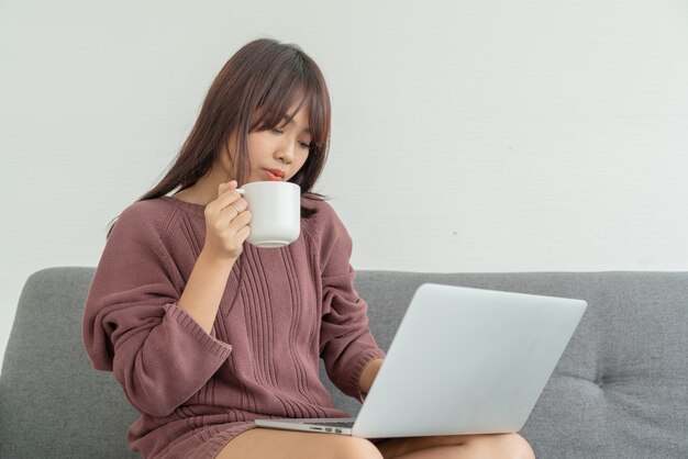 Mulher asiática usando laptop no sofá na sala de estar