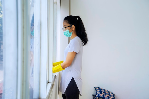 Mulher asiática usando líquido desinfetante para limpar a janela