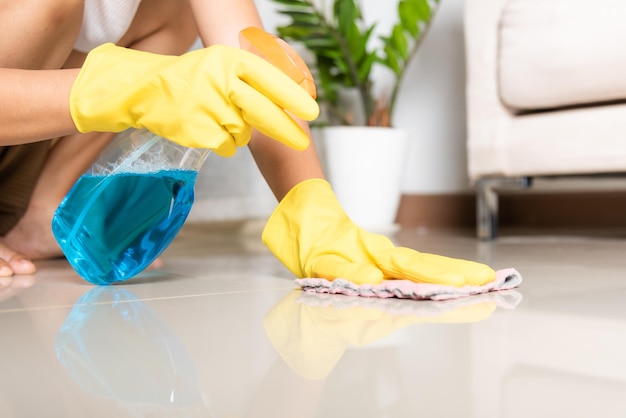 Mulher asiática usando luva de borracha amarela com pano de pano e piso de limpeza de spray detergente