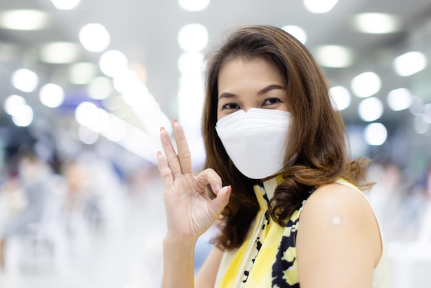 Mulher asiática usando máscara facial de higiene protetora pose feliz para a câmera depois de terminar de receber a vacina para coronavírus ou covid-19.