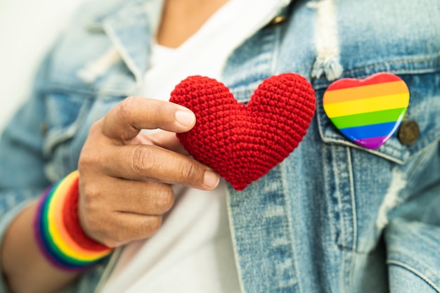 Foto mulher asiática usando pulseiras de bandeira arco-íris e segurando coração vermelho símbolo do mês do orgulho lgbt celebra anual em junho social de direitos humanos gays lésbicas bissexuais transgêneros